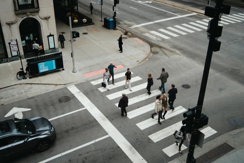 Aerial view of people crossing a city street at a pedestrian crosswalk, an image for The Scale of Leaving: Doubt in the Muslim World