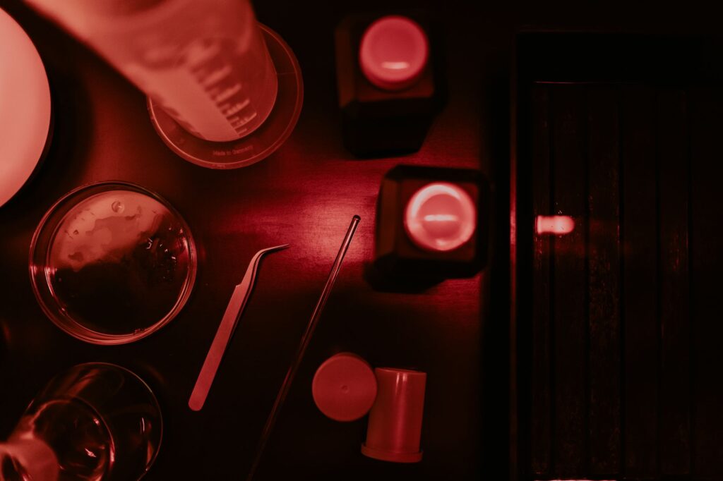 Close-up of darkroom equipment under red lighting, featuring flasks and tweezers.