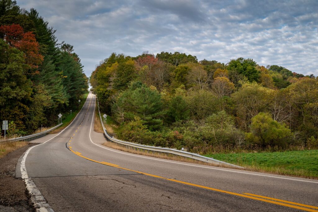 Curving road through lush autumn foliage under a cloudy sky.