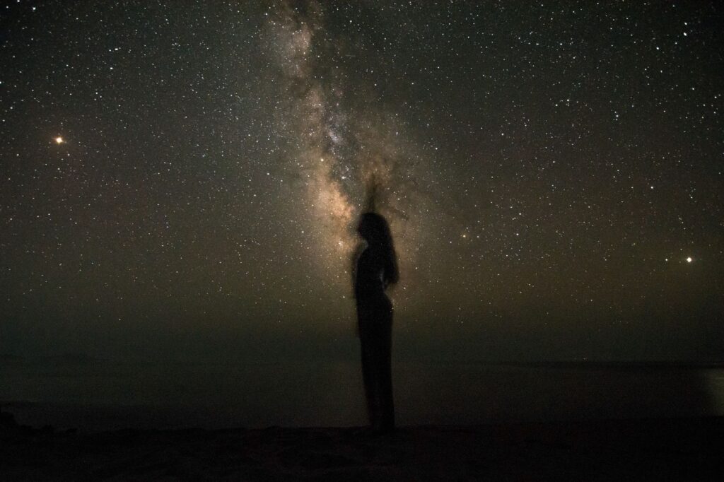 A silhouette stands under the expansive Milky Way in a clear night sky, showcasing the universe's beauty, an image for Angels and the Unseen: How Many Angels Are There