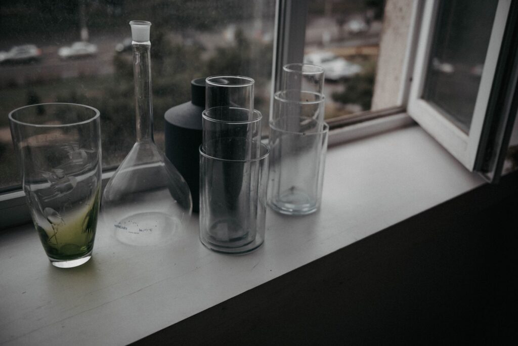 Group of glass vessels on a window sill with outdoor view.