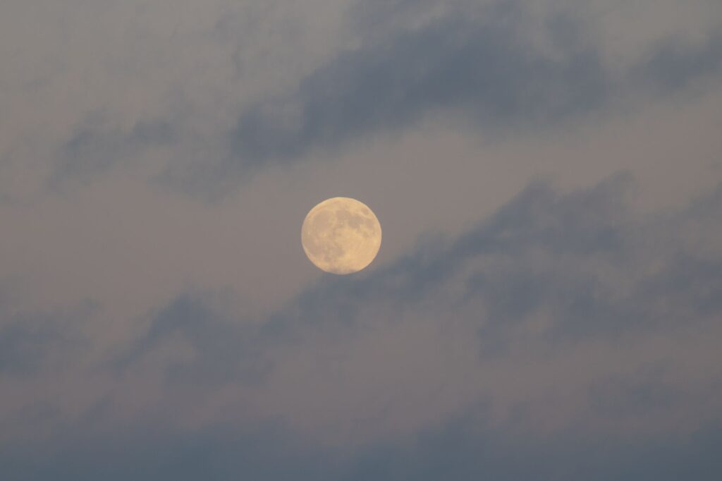 A tranquil full moon surrounded by soft, wispy clouds in a calm night sky.