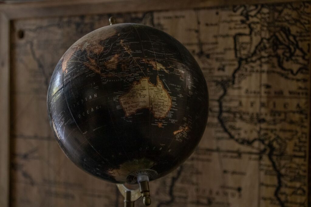 A vintage globe showcases Australia with a sepia world map in the background, offering a classic exploration theme, an image for The Religion of Your Birth: An Accident of Geography