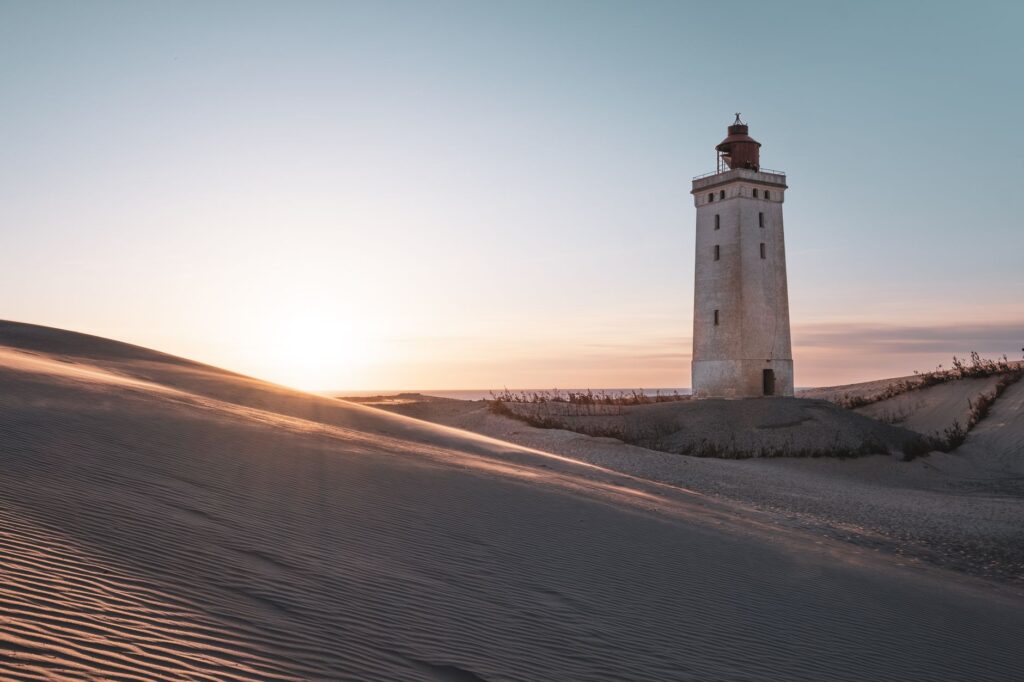 Scenic view of Rubjerg Knude Lighthouse surrounded by sand dunes during sunset in Løkken, Denmark.
