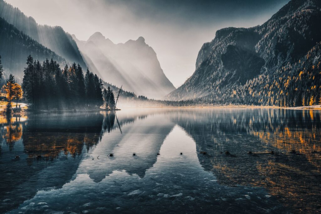 Serene view of a mountain lake with forest and reflections at dawn, creating a scenic and peaceful landscape.