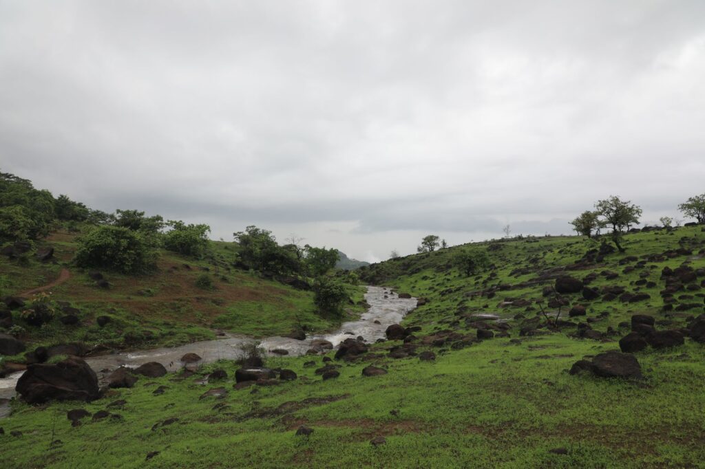 A scenic view of rolling green hills with a stream flowing through under a cloudy sky.