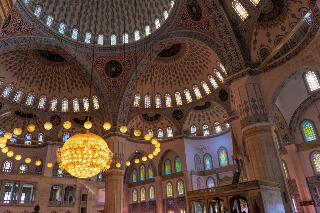 A grand view of an intricately decorated mosque interior featuring a stunning dome and chandelier.