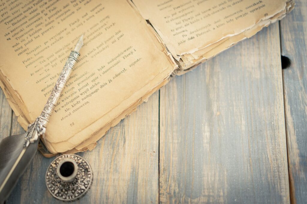 Close-up of an antique book with an ornate quill and ink pot on a wooden surface, evoking a classic vintage feel.