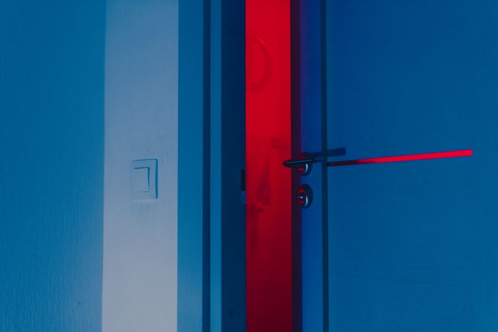 A half-open blue door illuminated by a dramatic red light reveals a unique interior atmosphere, an image for Apostasy: Why Can't People Leave Islam Without Consequences