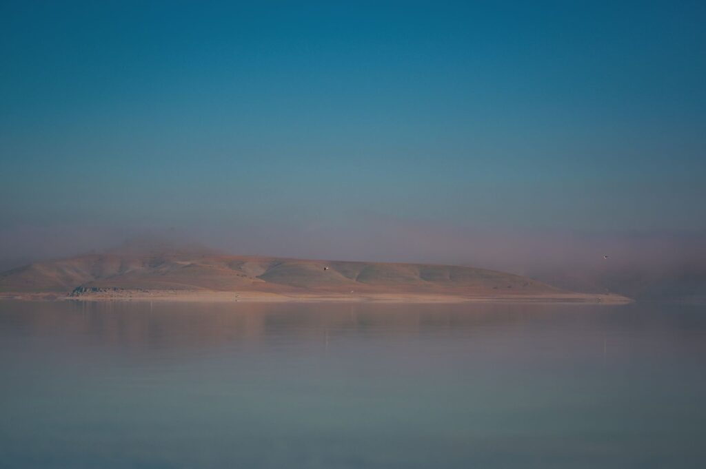 Peaceful misty landscape over calm water reflecting mountains at dawn.