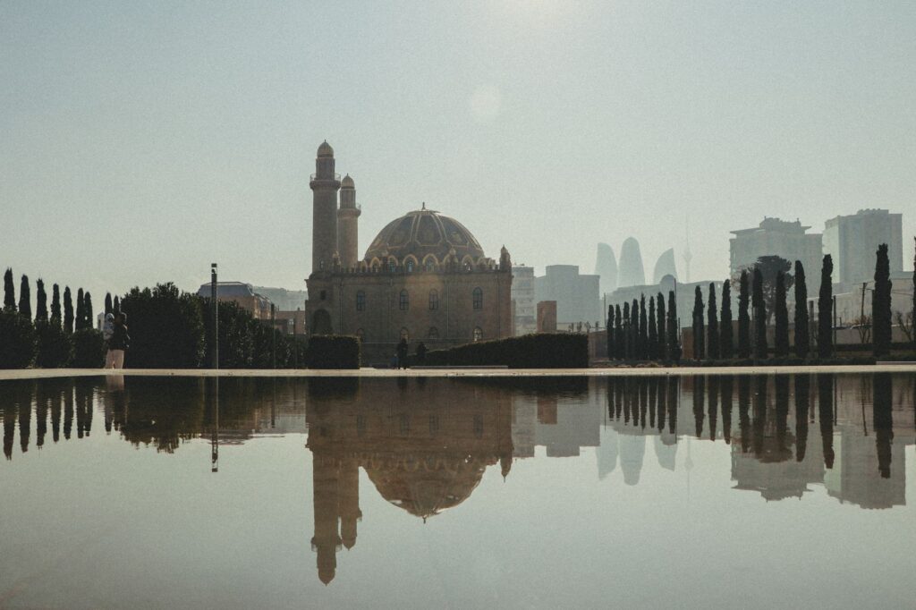 Elegant mosque reflection in a city reservoir with urban skyline backdrop.