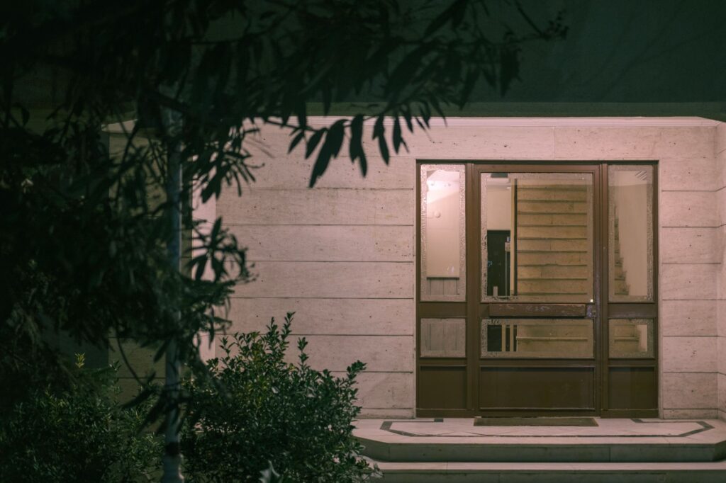 A serene nighttime view of a modern building entrance with surrounding foliage, creating a warm and inviting atmosphere, an image for Coming Back After Leaving: Is Return Possible