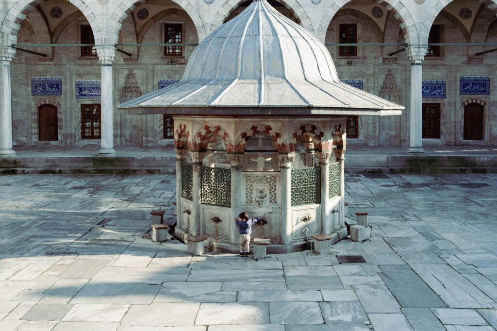 A child engaging with a fountain in a historic mosque courtyard in Istanbul, Turkey. Architectural beauty in a serene setting.