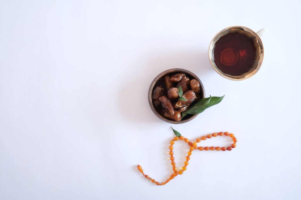 Overhead view of Ramadan iftar with dates, tea, and prayer beads on a white background.