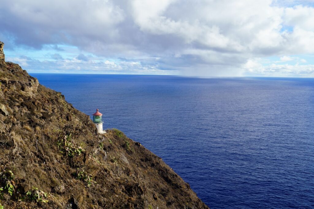 A picturesque lighthouse perched on a rugged cliff overlooking the vast ocean under a cloudy sky.