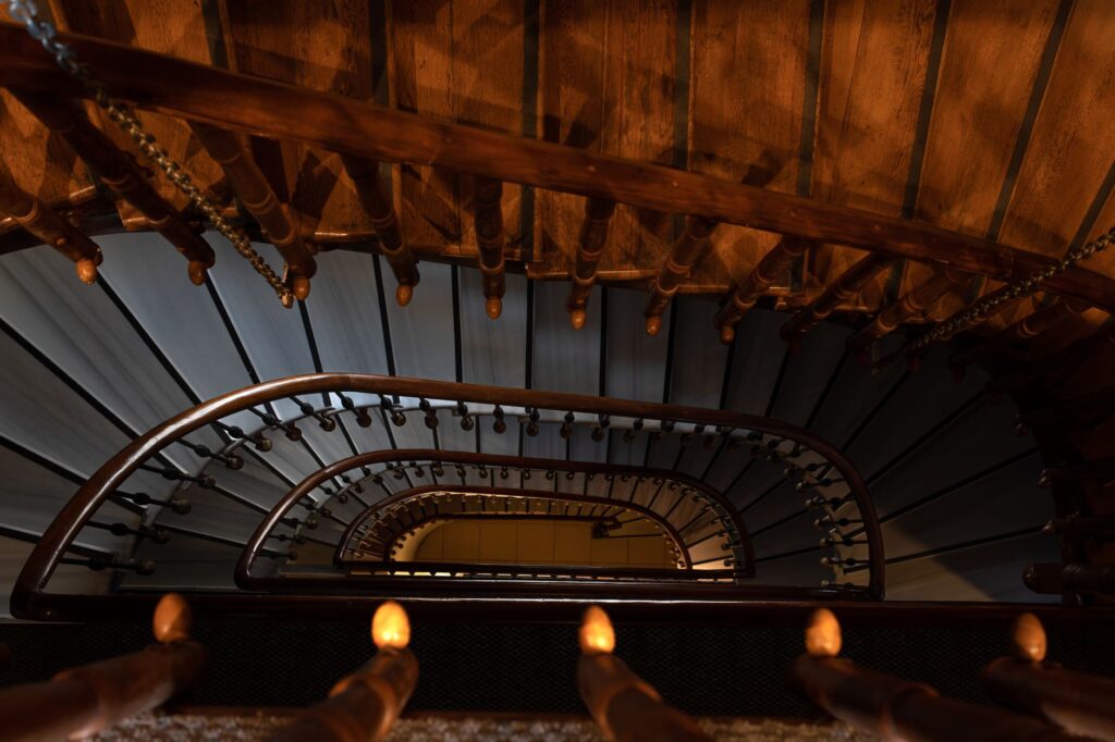 Top view of a dramatic spiral staircase with wooden rails and dark lighting.