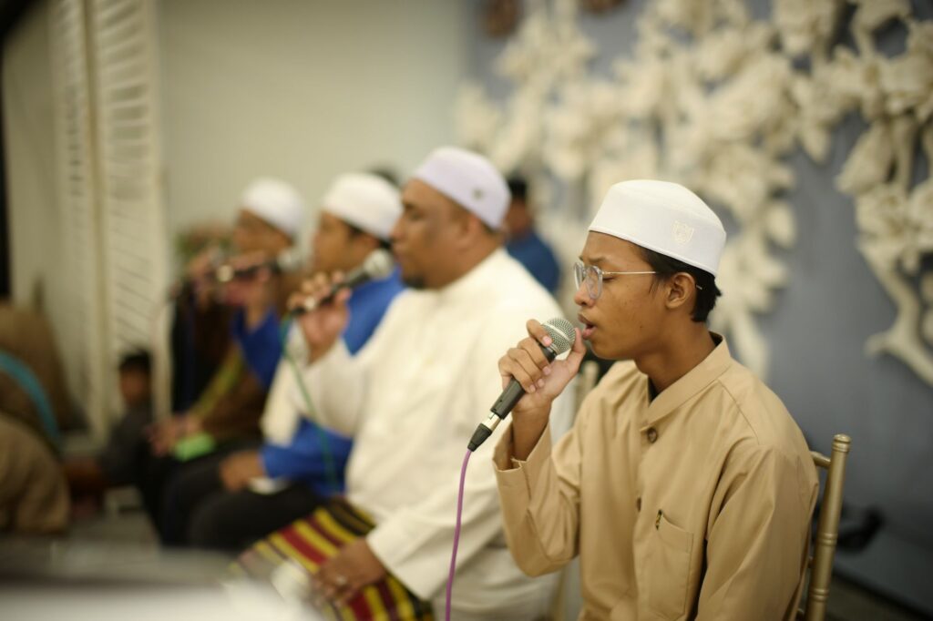 A group of Muslim men singing with microphones at a cultural event in Kuala Lumpur.