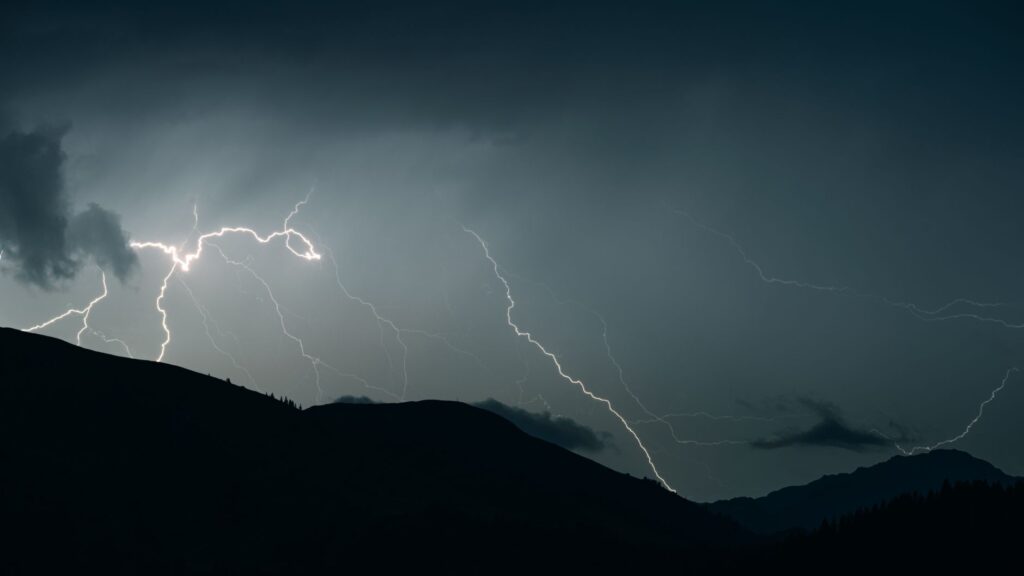 Captivating shot of lightning illuminating a dark sky over mountain silhouettes during a thunderstorm.