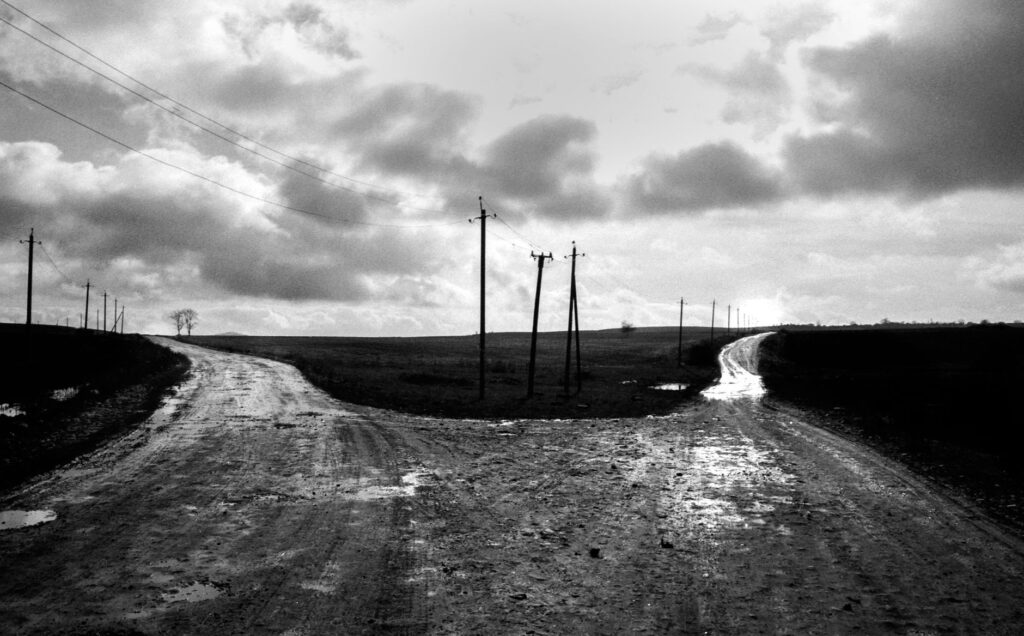 Monochrome image of a rural crossroad with utility poles under a cloudy sky, an image for The Dual Life: The Weight of Hidden Doubt
