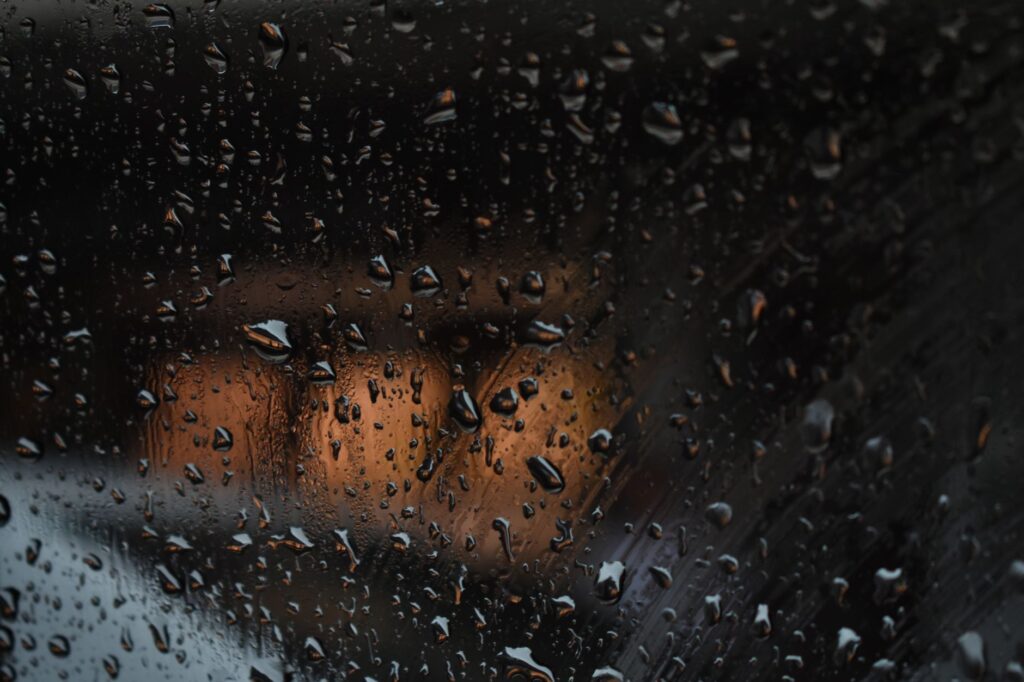 Close-up of rain droplets on a car window reflecting warm street lights at night.