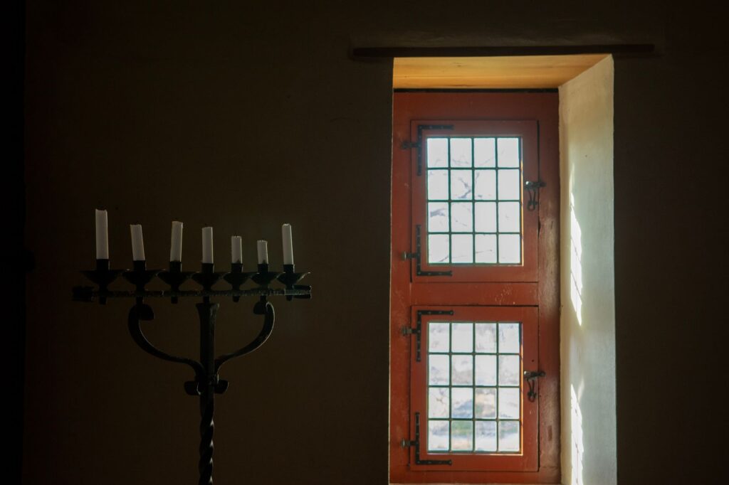 An antique candlestick set against a sunlit rustic window in an old building.