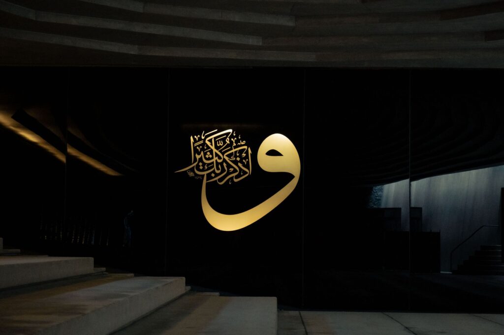 Elegant Islamic calligraphy in gold on a modern black wall, featuring architectural elements and stairs, an image for Arabic: Why Is God's Final Message in Arabic