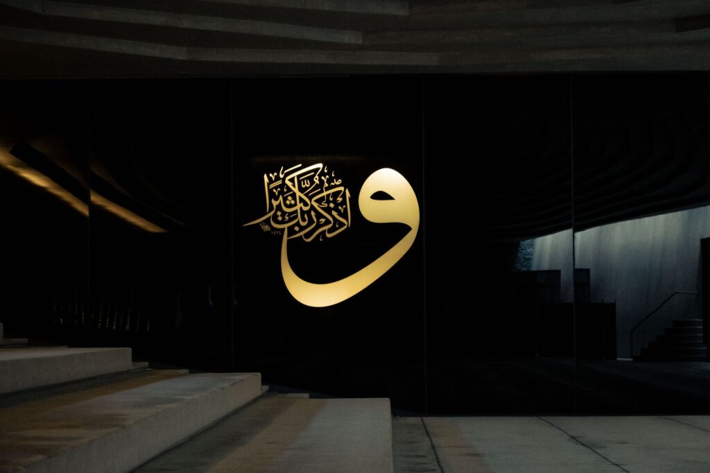 Arabic calligraphy art in Sancaklar Mosque wall, Turkey, illuminated in a dark indoor setting.