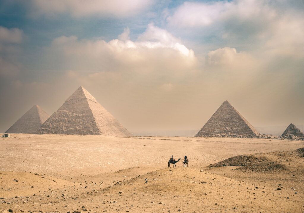 Explore the majestic Pyramids of Giza under a sunny sky with distant travelers on camels, an image for Did the Quran Move Haman From Persia to Egypt