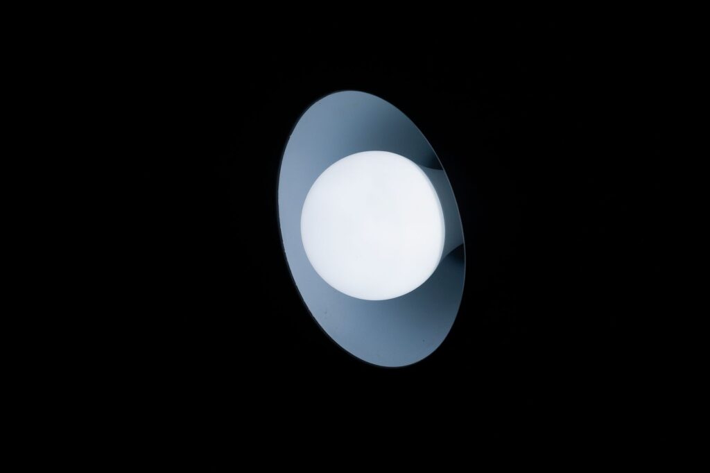 A minimalist circular overhead light emitting a soft glow in a dark room, highlighting contrast.