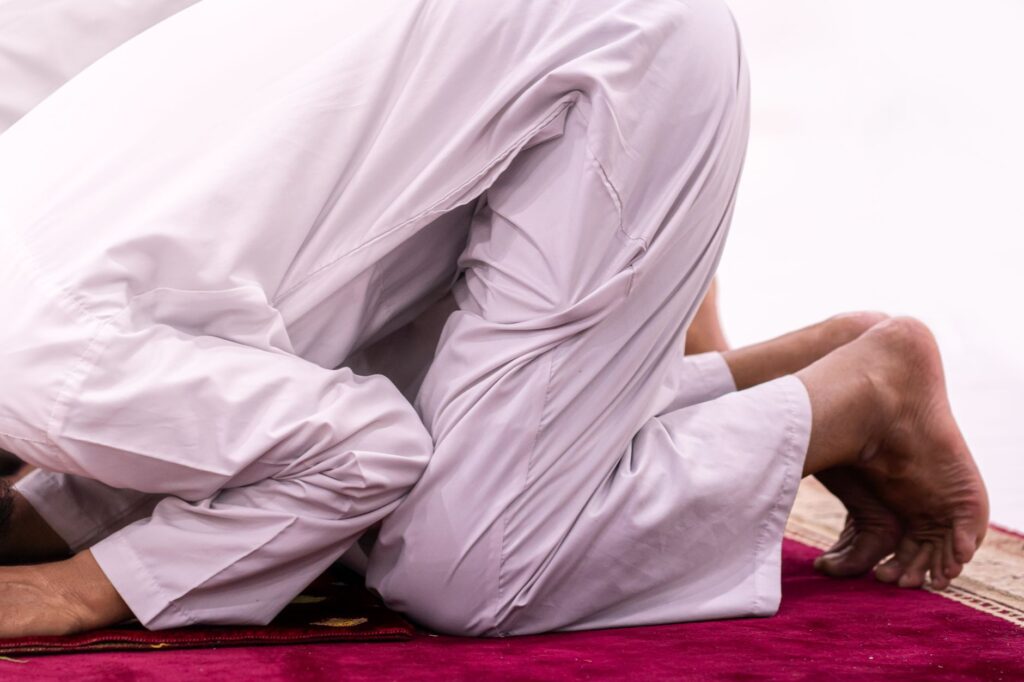 Close-up of a Muslim person in prayer position on a red carpet in Sulawesi Selatan, Indonesia, an image for Compelled Worship: Why Would God Need to Be Worshipped