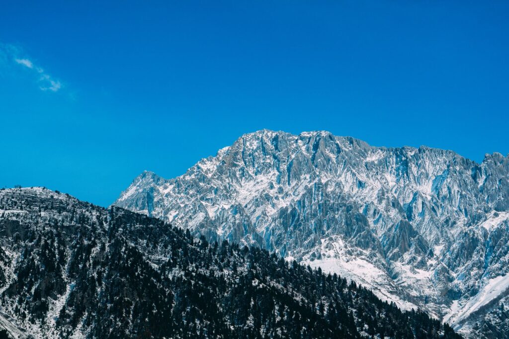 Dramatic winter scene of snow-capped mountains against clear blue sky, showcasing nature's beauty.