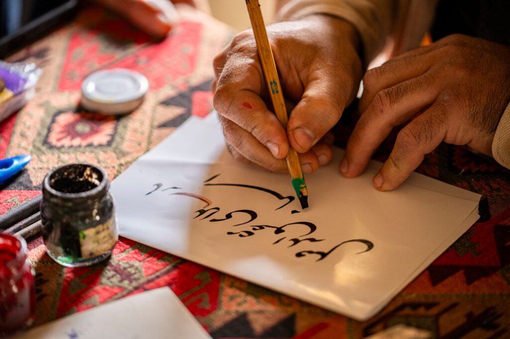 Hands writing traditional calligraphy with a pen on paper, showcasing cultural artistry in Baku.