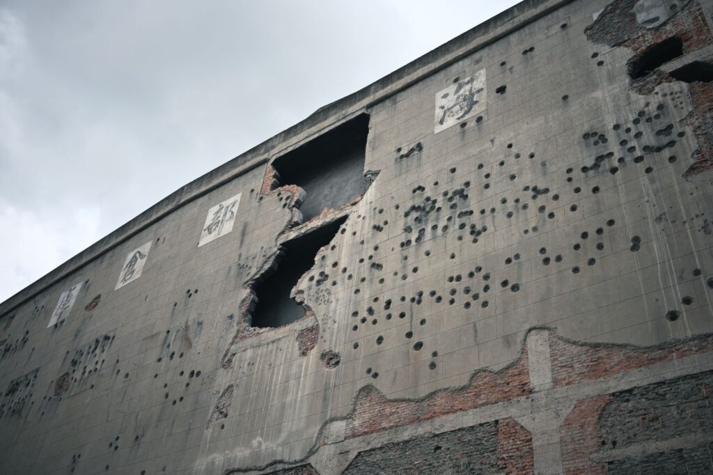A damaged building facade showing signs of war and decay under a cloudy sky.