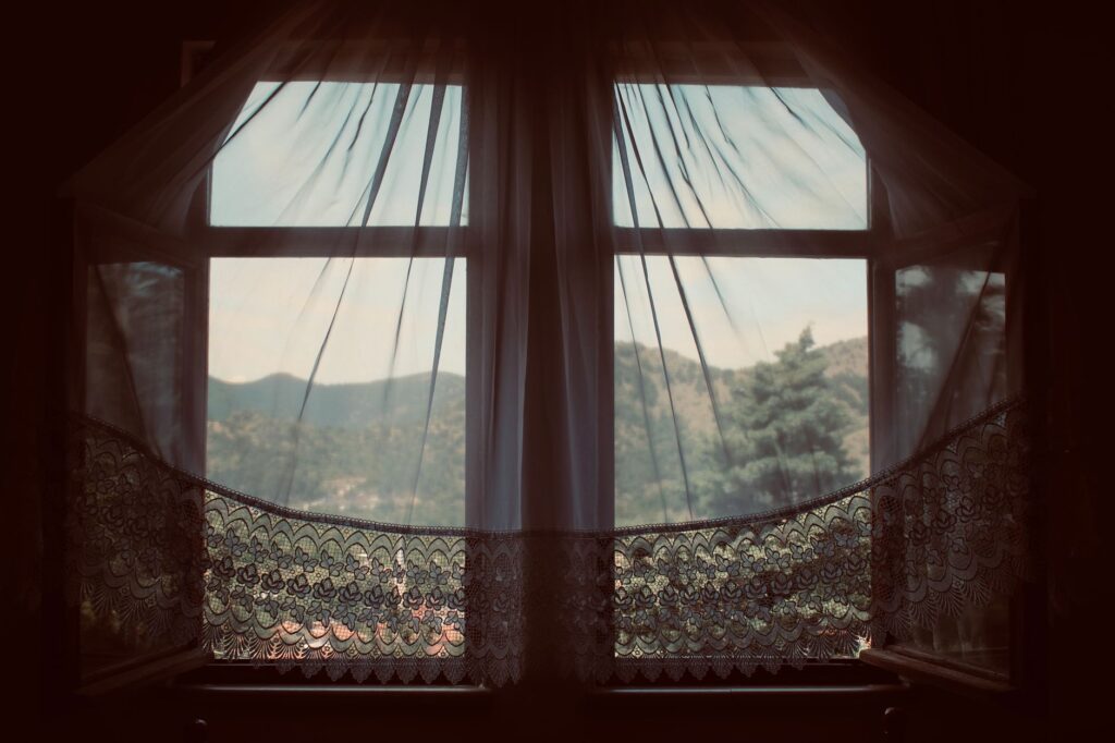 Serene landscape through a vintage window with lace curtains, capturing the peaceful outdoors.