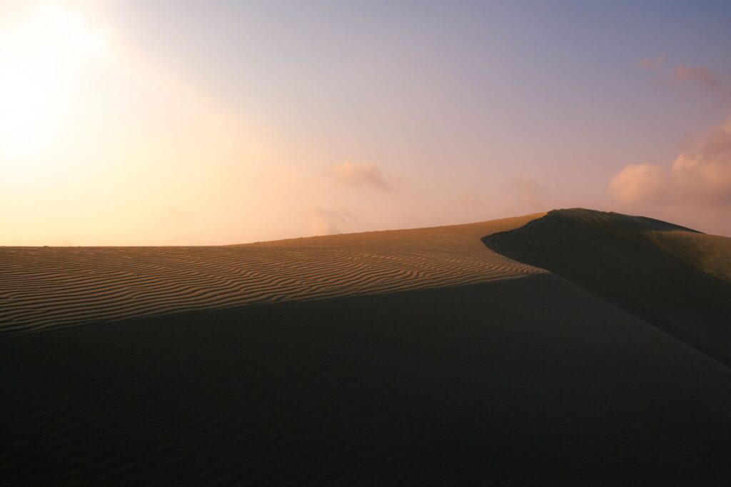 Golden sand dunes with ripples under a stunning sunset sky, creating a serene and tranquil atmosphere.