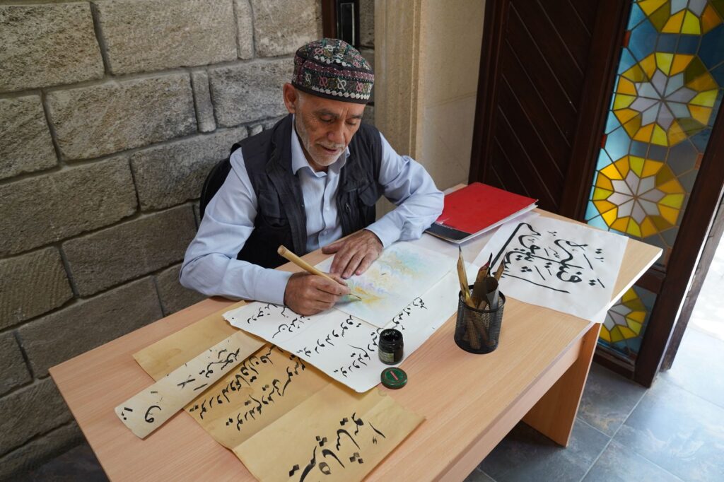 An elderly man skillfully creates traditional Arabic calligraphy with a brush and ink indoors.
