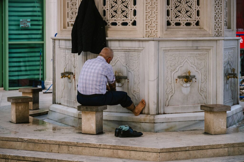 An elderly man performs ablution at a mosque fountain, showcasing cultural traditions.