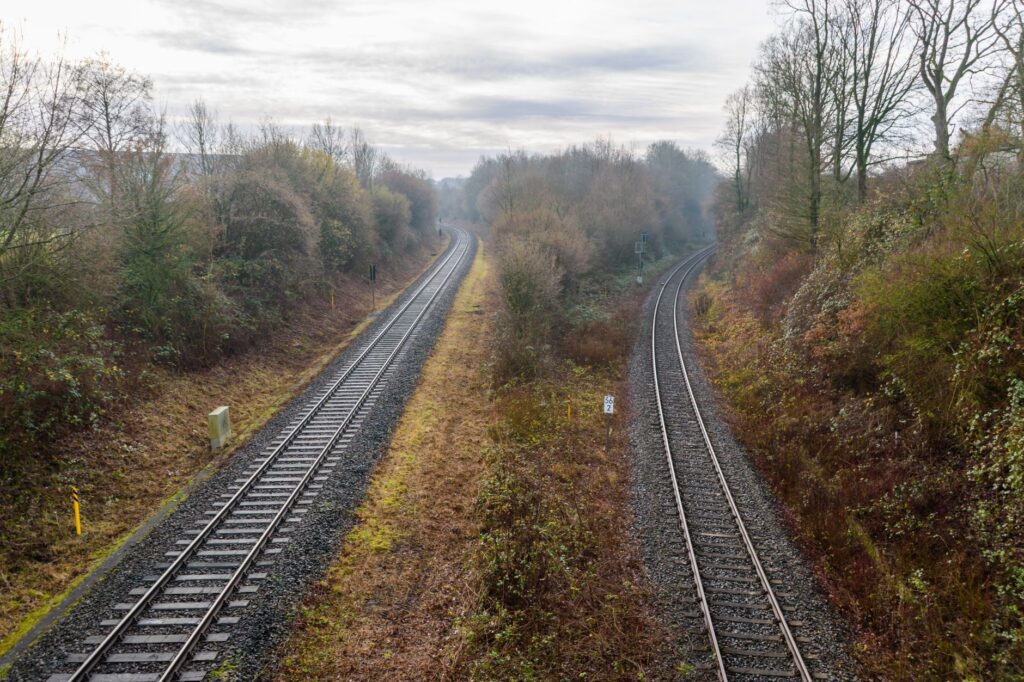 A serene view of parallel railroad tracks surrounded by autumn foliage on an overcast day.