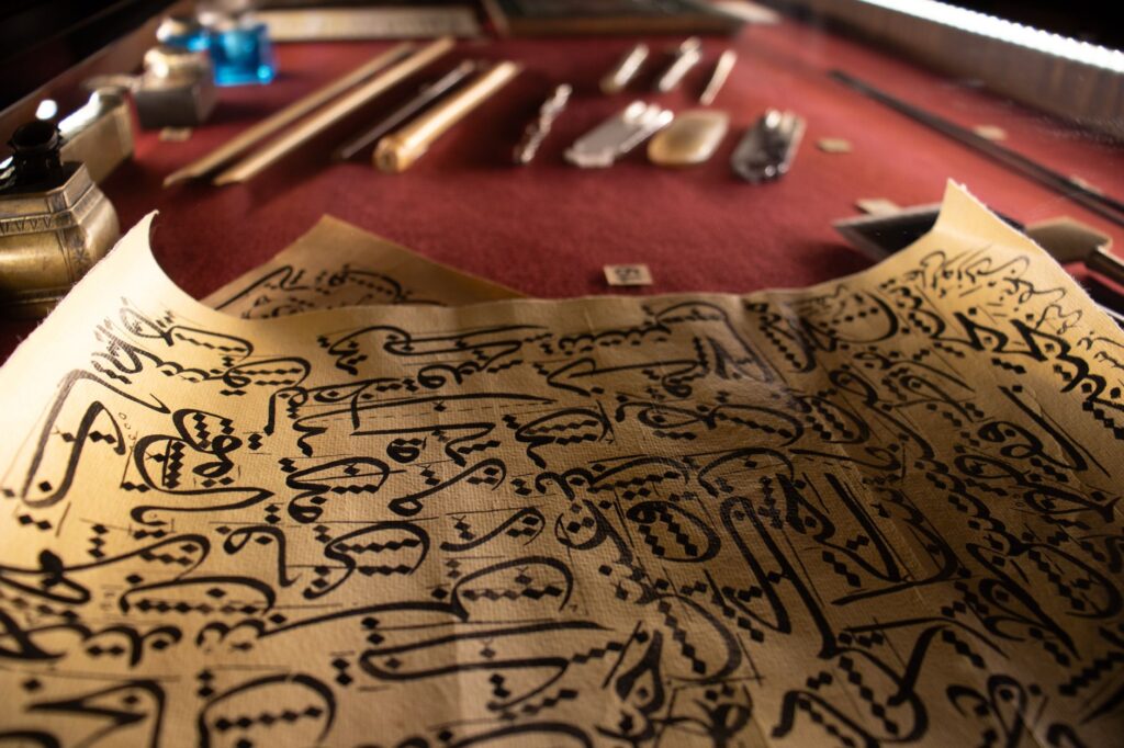 Close-up of intricate calligraphy on parchment with antique writing tools on a wooden desk.