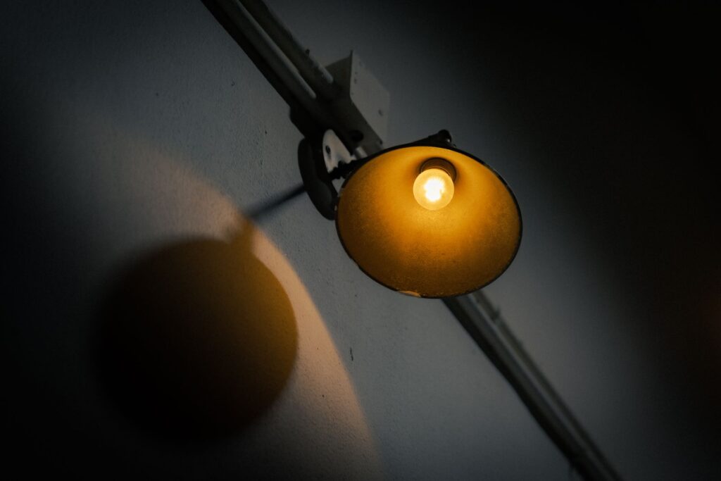 A single wall-mounted light casts a warm and moody ambiance in a dark indoor setting, an image for Shirk: Why Is It the One Unforgivable Sin