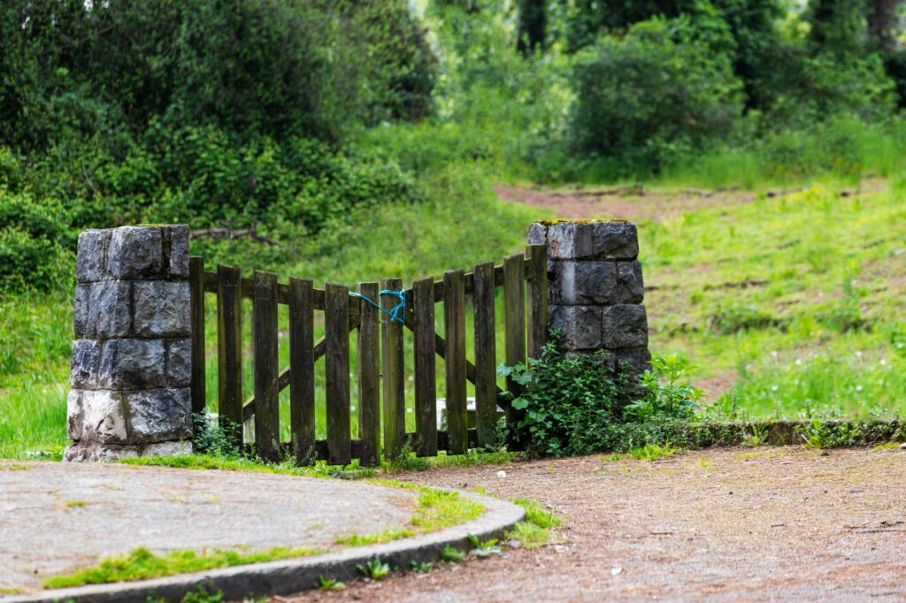 A rustic wooden gate with stone pillars in a lush green outdoor setting.