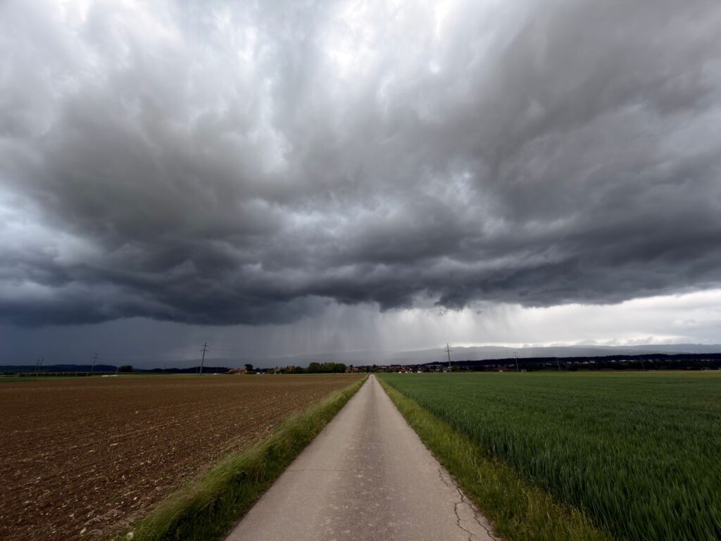 Looming storm clouds over a rural path and fields in Swiss countryside.