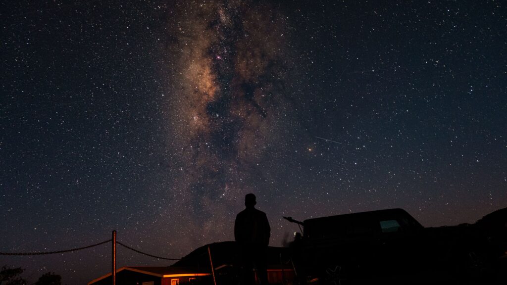 A person silhouetted against the stunning backdrop of the Milky Way and a starry night sky.