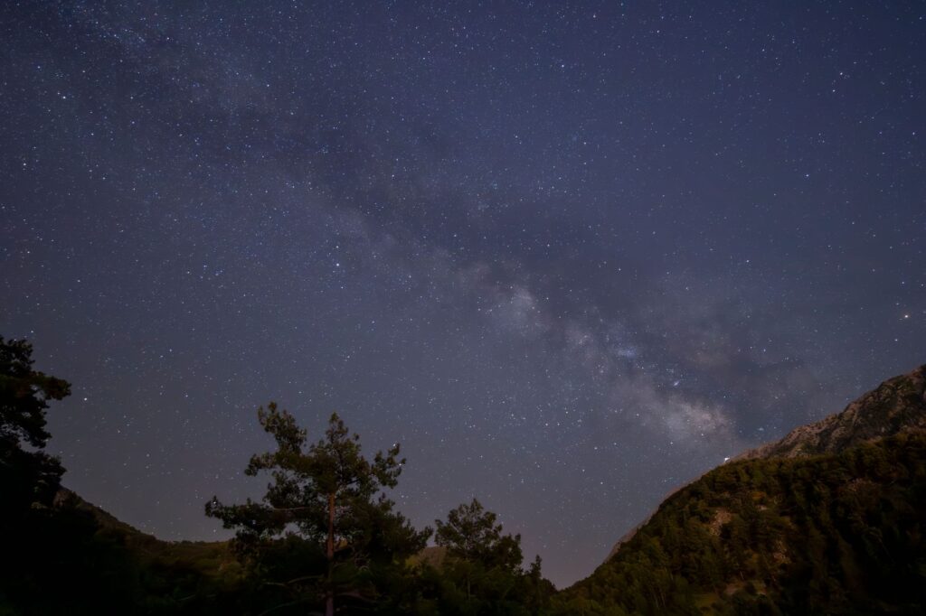 A stunning view of the Milky Way galaxy visible above darkened mountain landscape and trees, an image for Why Does Anything Exist Rather Than Nothing