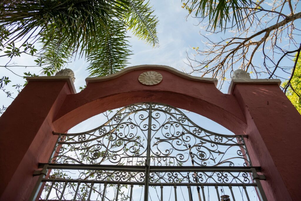 Ornate iron gate framed by palm trees, under blue sky, in Campinas, Brazil.