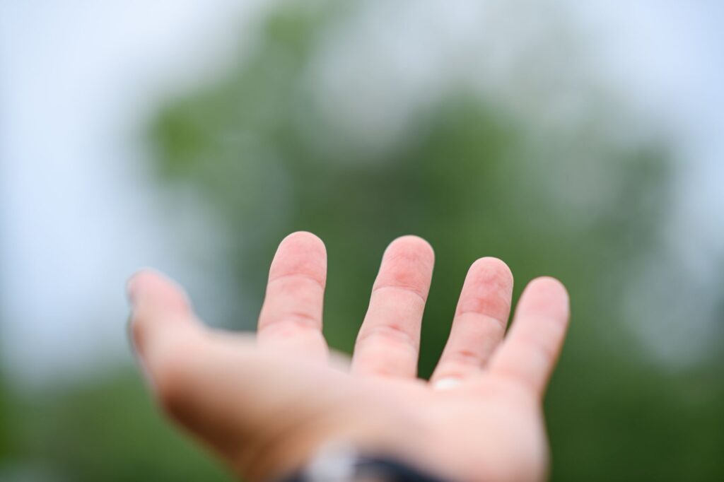 Close-up of an outstretched hand against a soft-focused background of greenery, symbolizing connection, an image for Ethics and Morality Without Religion: What Grounds Them