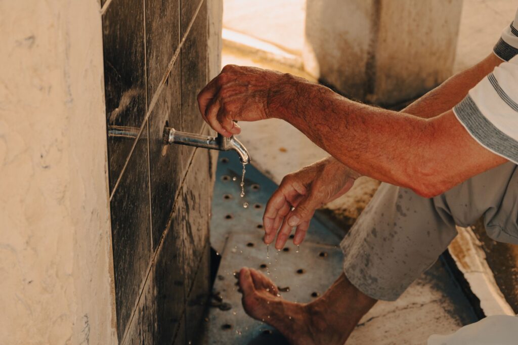 A man performing wudu, the ritual washing before Islamic prayers, at a water source, an image for Too Many Rules? Why Islam Regulates Trivial Things