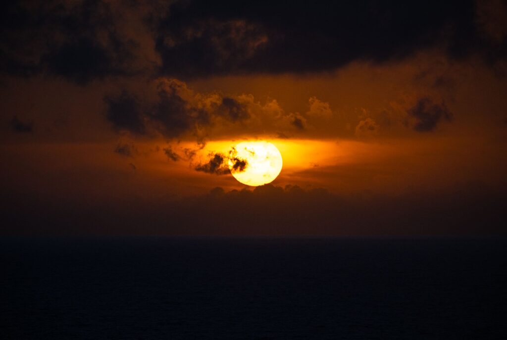A breathtaking view of a fiery sunset over the ocean, casting a warm glow and dramatic clouds.