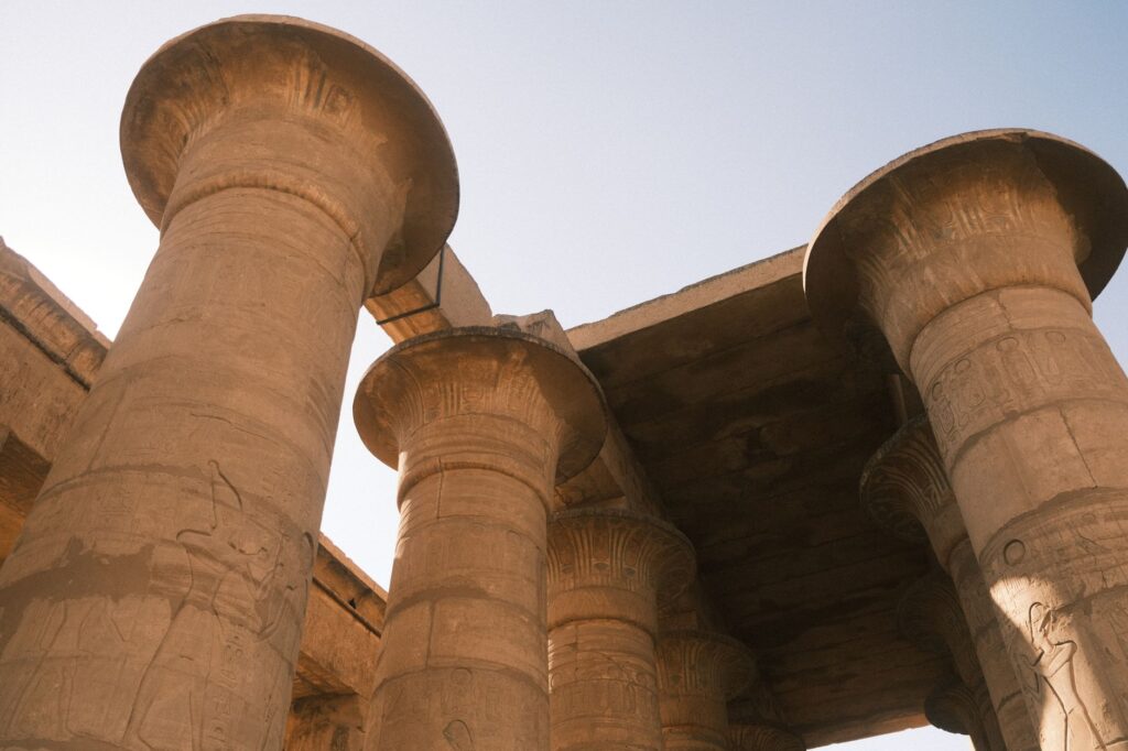 Majestic ancient Egyptian columns in weathered stone under clear sky.