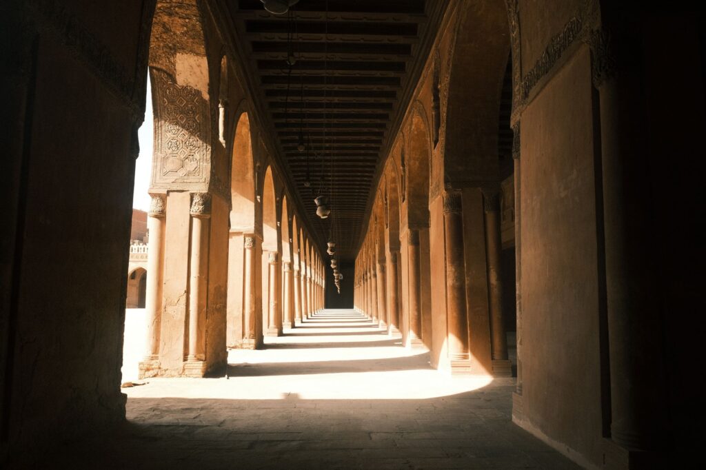 Sunlit corridor of a historic mosque in Cairo, showcasing arches and intricate architecture.